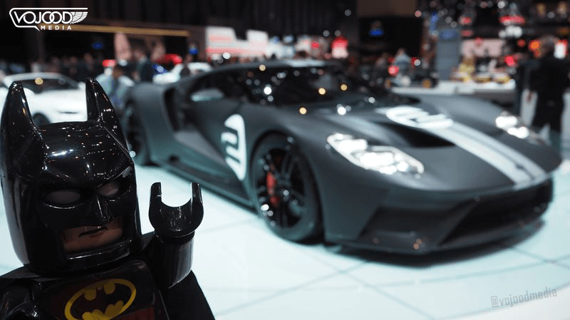 Figurine Lego Batman au premier plan avec une voiture de sport grise en arrière-plan au Salon International de l'Automobile de Genève
