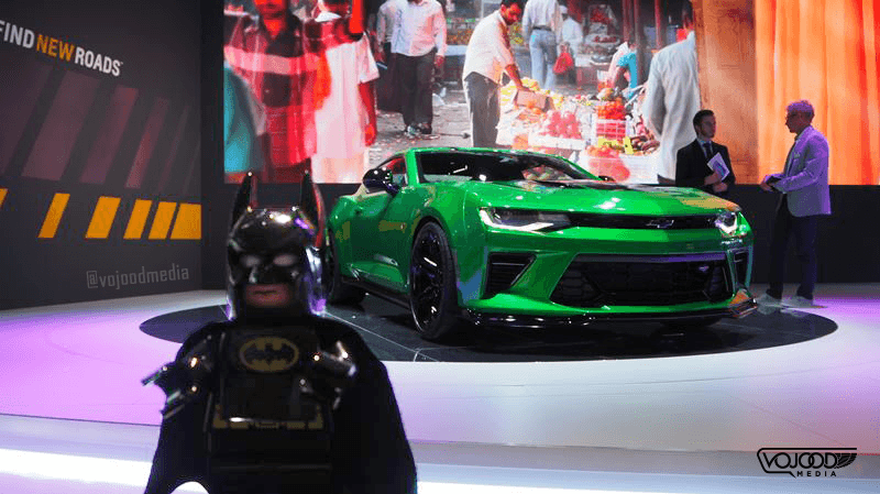 Batman en costume face à une Chevrolet Camaro verte au Salon International de l'Automobile de Genève