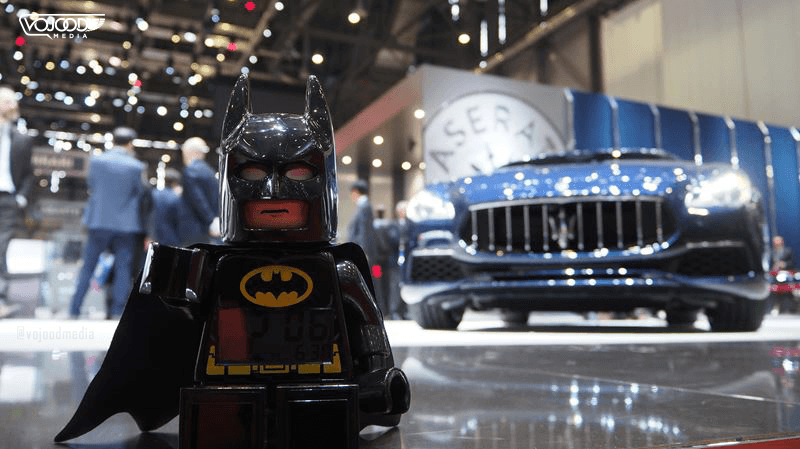 Figurine Lego de Batman au premier plan, face à une voiture noire au Salon International de l'Automobile de Genève