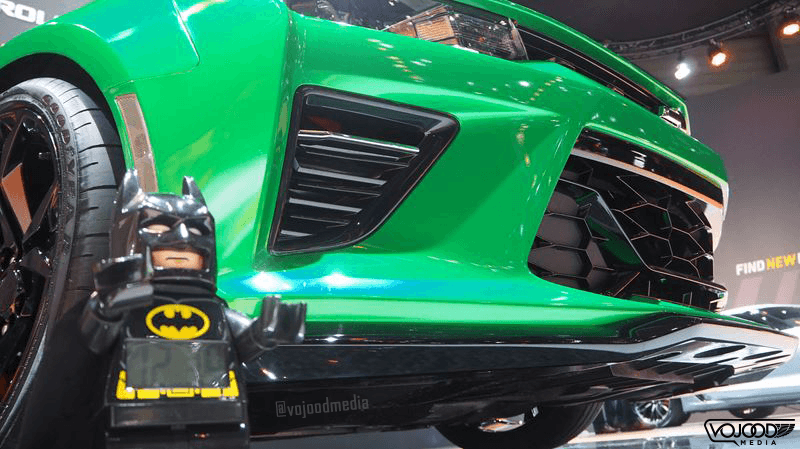 Figurine Batman jaune et noir devant une voiture sportive verte fluo au Salon de Genève