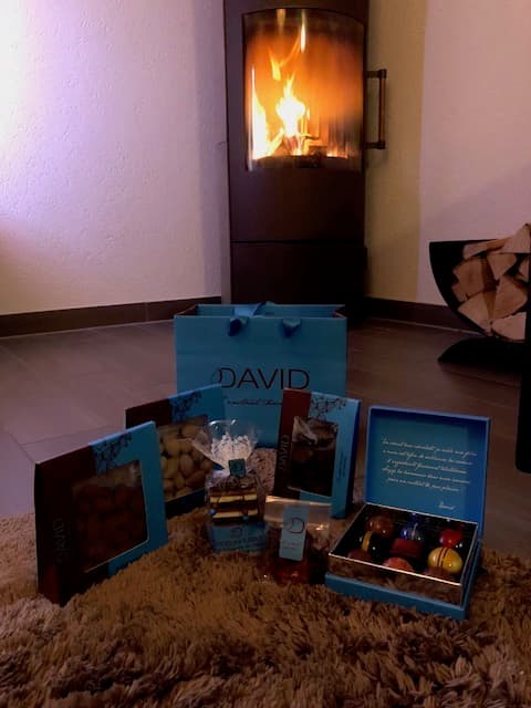 Présentoir bleu de la boutique David l'Instant Chocolat avec produits et emballages, devant une cheminée allumée