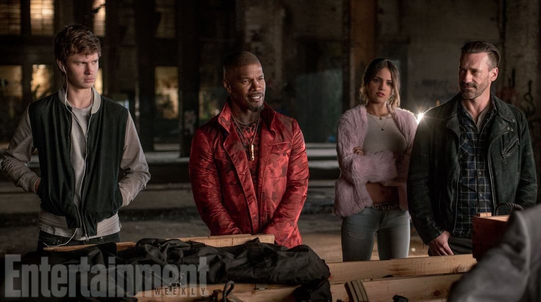 Quatre personnages debout dans un entrepôt sombre, penchés autour d'une table en bois, scène du film Baby Driver