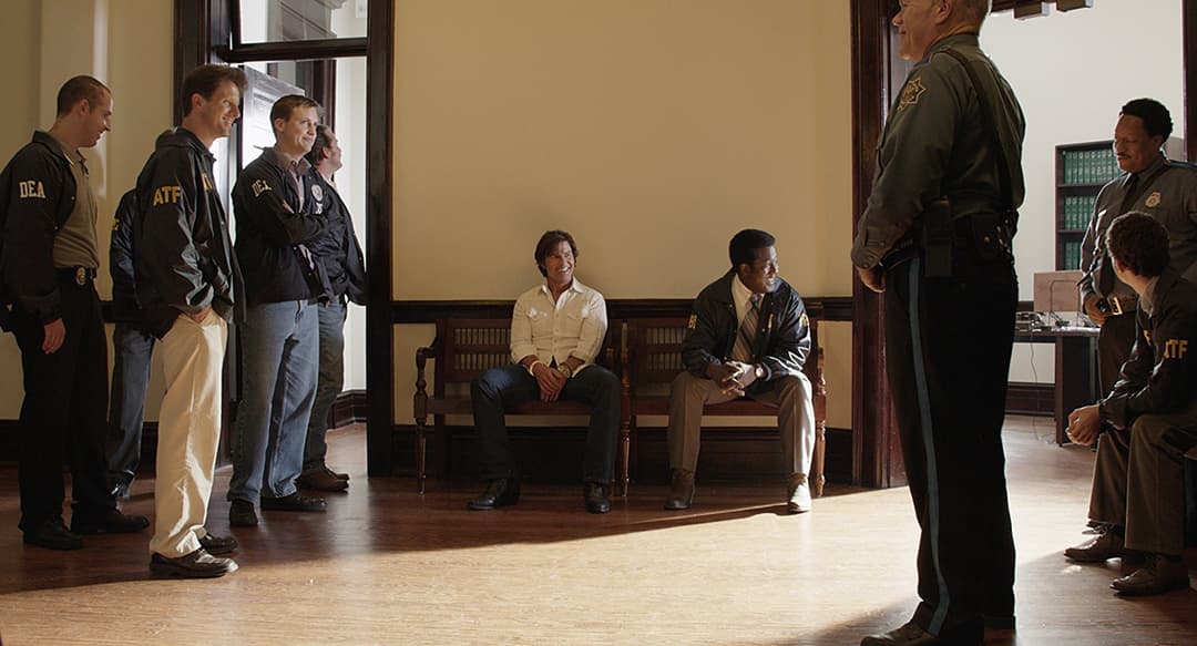 Tom Cruise assis entre des agents fédéraux en uniforme dans un interrogatoire dans Barry Seal : American Traffic