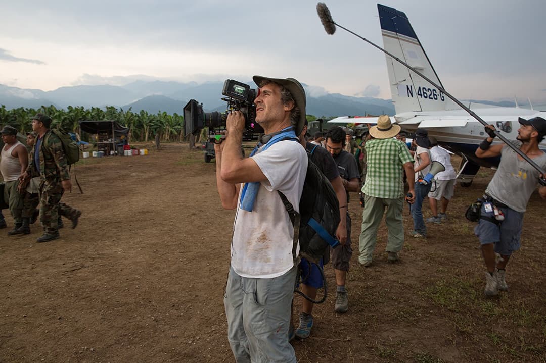 Caméraman filmant sur un terrain d'atterrissage improvisé avec avion et montagnes en arrière-plan
