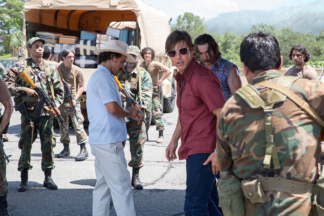 Tom Cruise en chemise bordeaux, lunettes de soleil, discute avec des militaires armés près d'un camion de ravitaillement en montagne