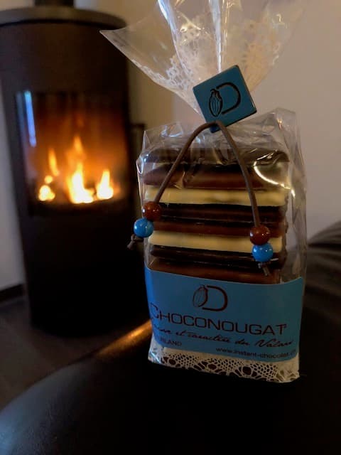 Choconougat de David l'Instant Chocolat en sachet transparent, alternant nougat et chocolat, devant un feu de cheminée