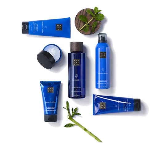 Produits de cosmétiques Rituals bleus et flacons disposés avec plantes vertes, incluant gel, crème et spray