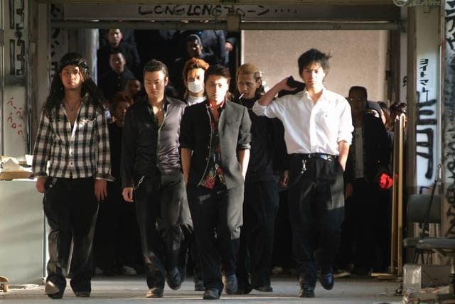 Groupe de jeunes hommes marchant dans un couloir d'école, vêtus de blazers et chemises, dans une scène du film Crows Zero