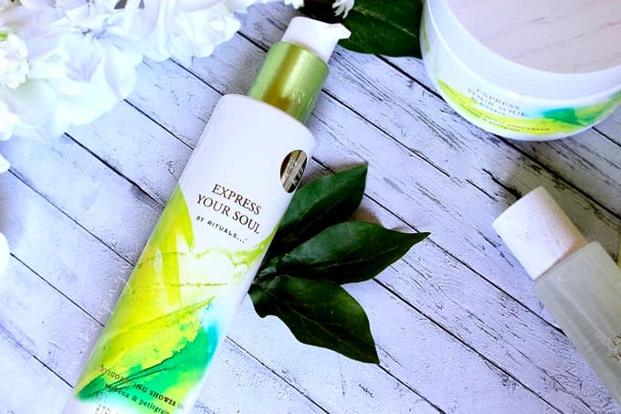 Flacon Express your Soul Shower Oil de RITUALS avec pompe, aux nuances vert et blanc, entouré de feuilles vertes sur un fond gris