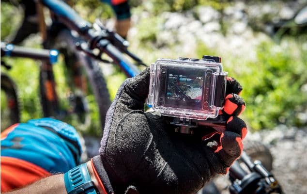 Action cam avec boîtier étanche transparent et écran tactile LCD, tenue à la main avec gants noirs lors d'une sortie outdoor