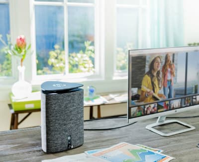 Enceinte intelligente noire et grise avec couvercle acoustique, posée sur bureau près d'écran et fenêtre ensoleillée