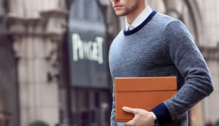 Homme en pull bleu gris tenant un ordinateur portable Huawei MateBook de couleur orange sous son bras