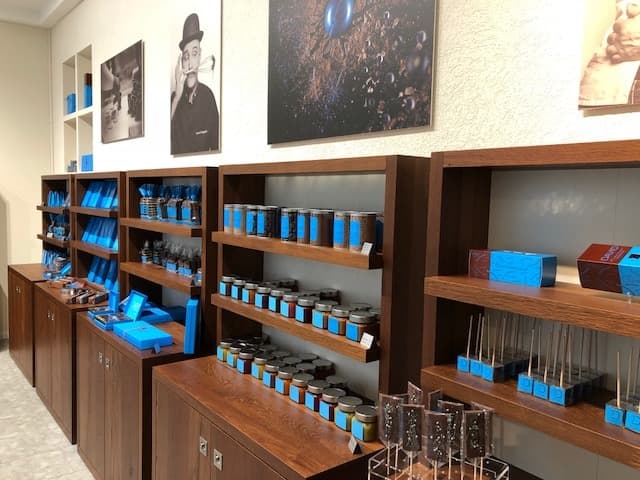 Boutique de chocolaterie avec meubles en bois massif, étagères remplies de produits bleus et noirs, comptoir de dégustation et photos encadrées aux murs
