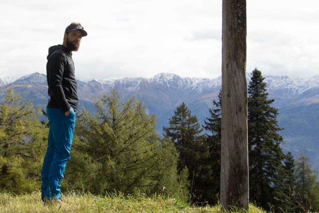 Homme en pantalon trekking bleu ODLO SOLITUDE en montagne, vue sur les Alpes enneigées