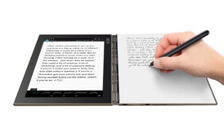 Tablette à écran tactile affichant un texte avec stylet, à côté d'un carnet blanc sur lequel une main écrit avec un stylet noir
