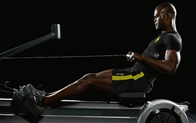 Homme torse nu portant un t-shirt noir avec détails jaunes, utilisant un équipement de fitness technologique sur fond noir