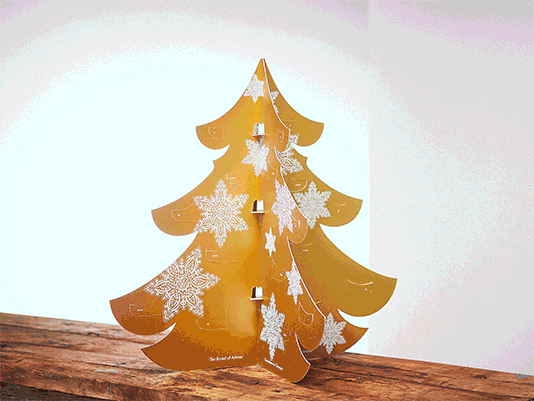 Calendrier de l'Avent Rituals en forme de sapin doré ajouré avec flocons de neige et petites portes, posé sur bois