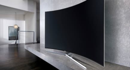 Télévision Samsung incurvée 4K avec contours métalliques posée sur un meuble blanc dans un salon moderne