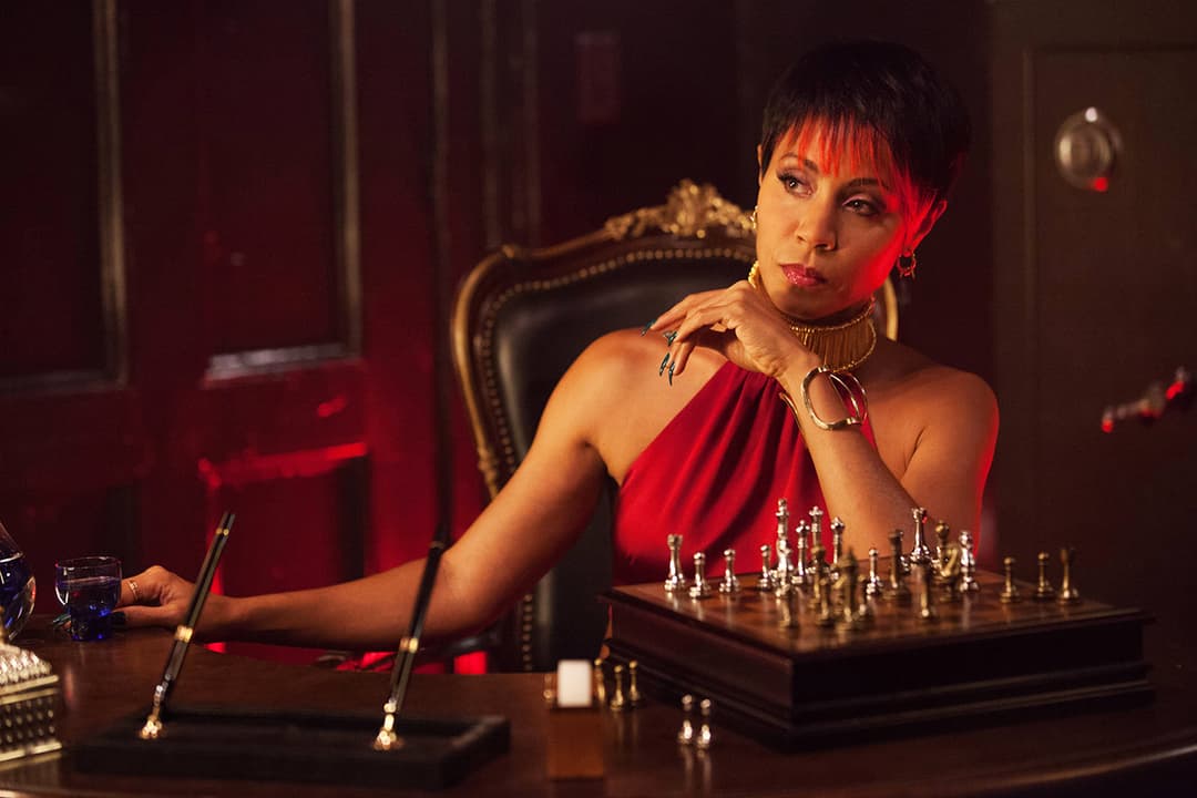 Femme en robe rouge assise à un bureau dans une ambiance sombre et rouge, jouant aux échecs